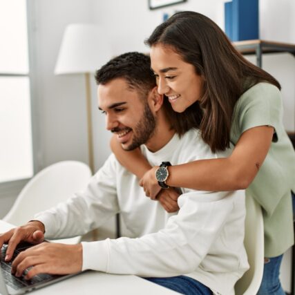 Young latin couple using laptop and drinking coffee at home.
